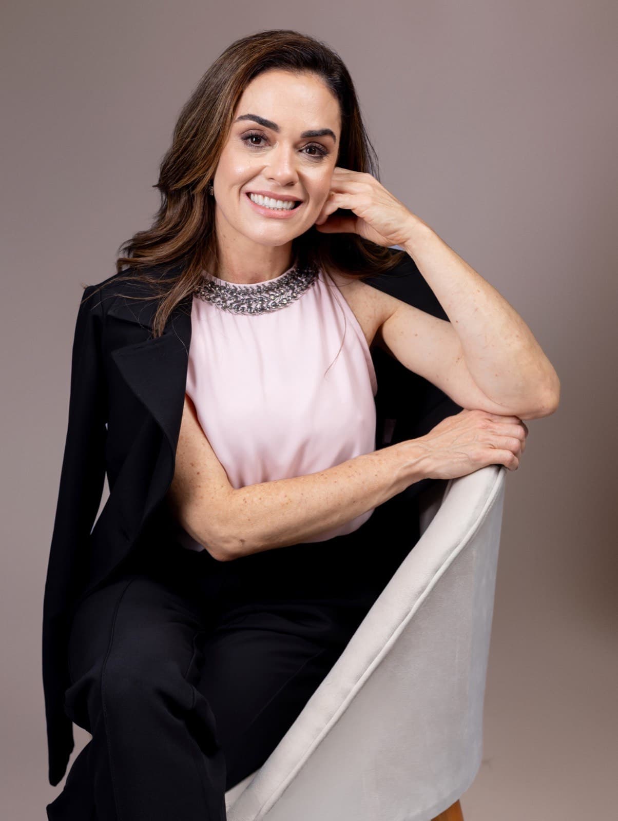 Dra. Lizéta Cristine Lemes Saúde sentada, retrato de corpo inteiro em fundo neutro